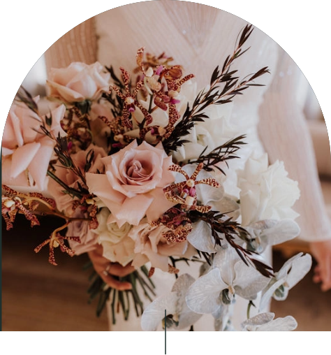 A bride is holding her bouquet of beautiful flowers they are a pink and white with green through out the design 
