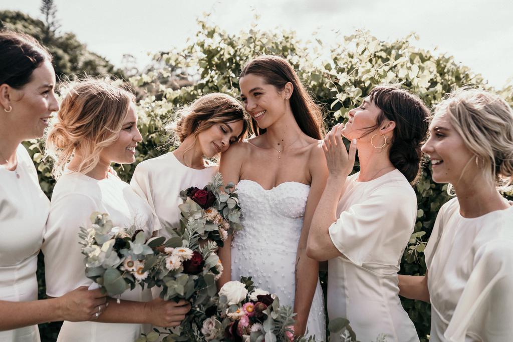 A group of girls all dressed in white looking at the bride in white