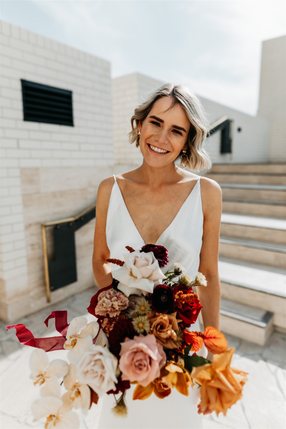 A women holding up a bouquet of coloured flowers and roses in her wedding dresss
