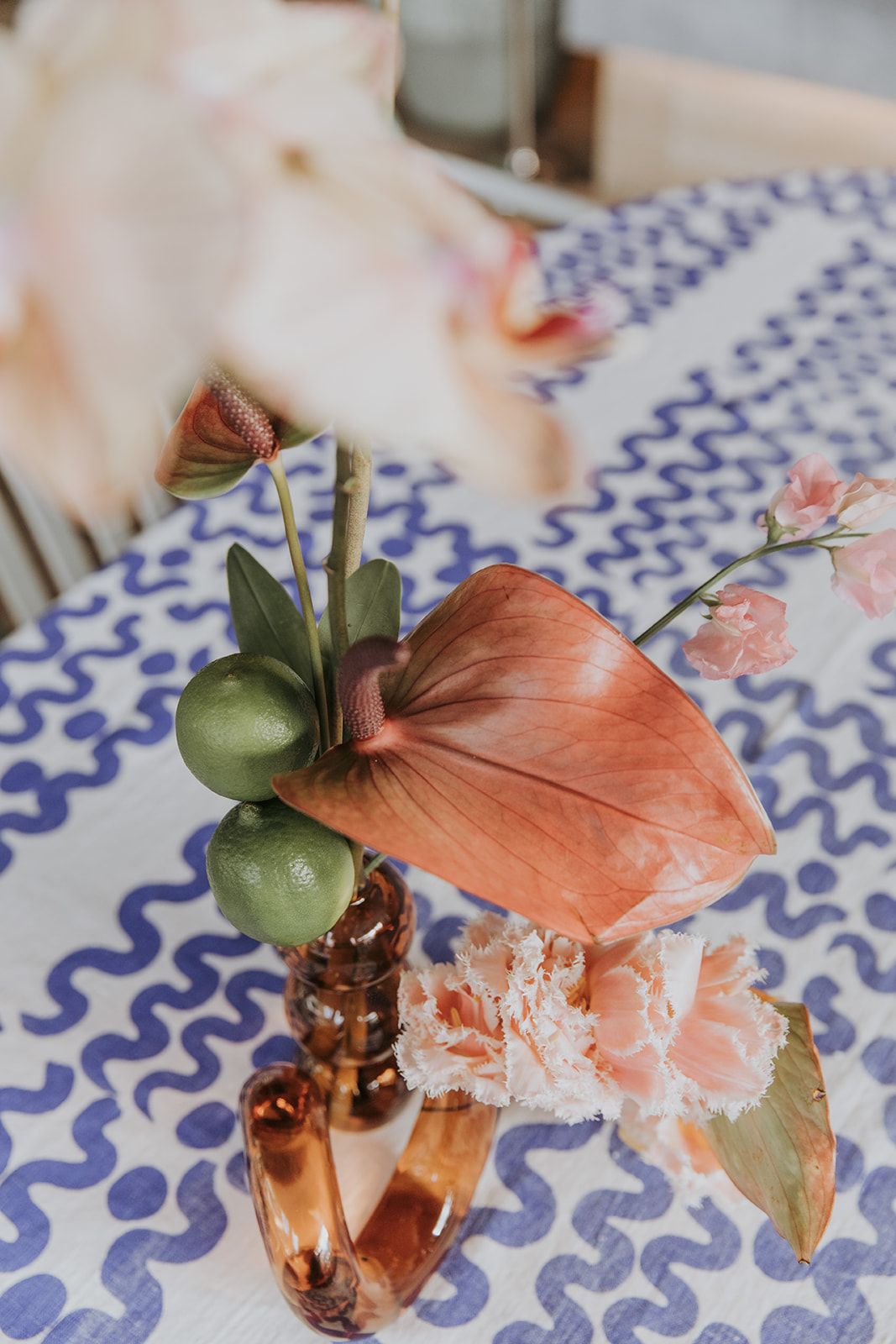 A close up photo of a flower holder and pink flowers with limes and lillys. The table has blue and white patterns