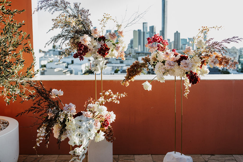 Orange background and a view of the city in the background with dried flowers and whtie roses, and red flowers.